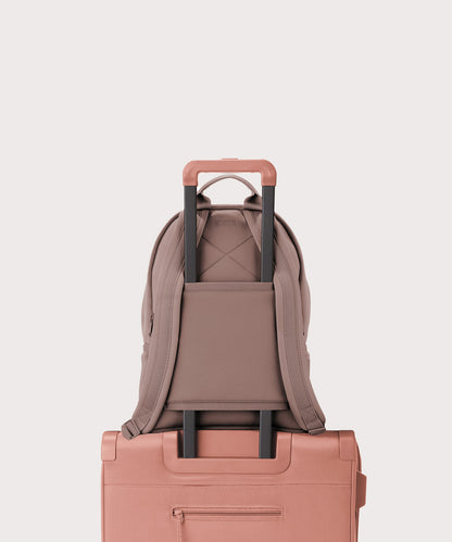 Dagne Dover medium Dakota Neoprene Backpack in pink strapped to luggage with the neoprene luggage-handle sleeve.